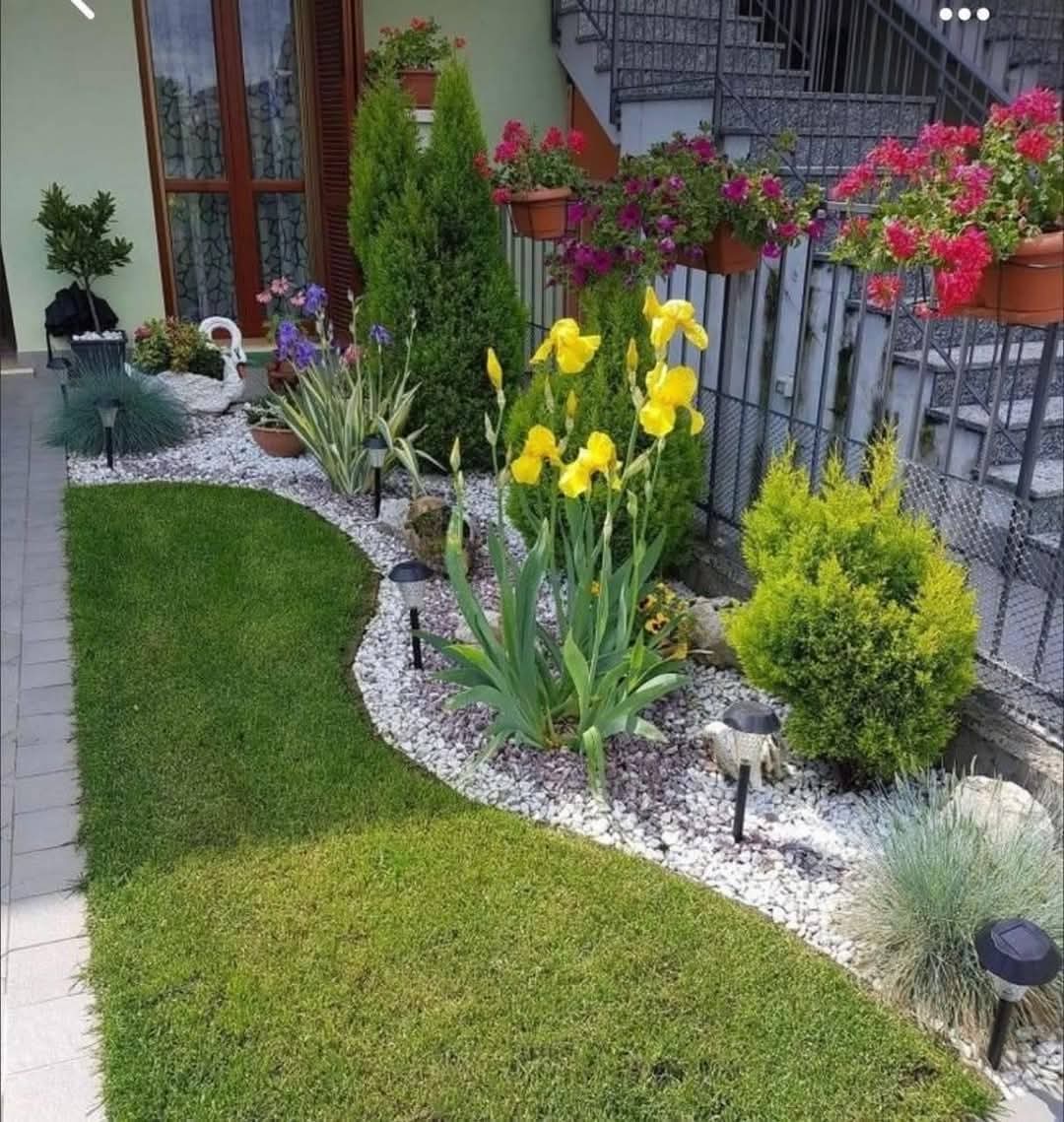 Landscaped garden bed with white pebbles, shrubs, flowers and solar lights beside a lawn